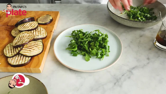 Arrange the grilled eggplant slices over the dressed rocket salad.