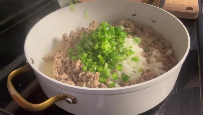 Add the chopped onion, green bell pepper, and red bell pepper to the pan with the sausage. Sauté briefly.