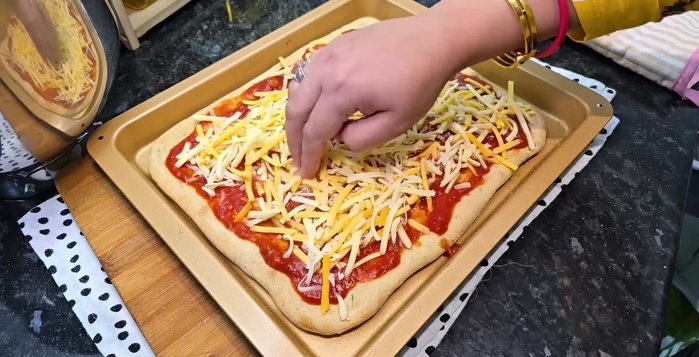 Add pizza sauce, cheese, and desired toppings to the pre-baked pizza base.
