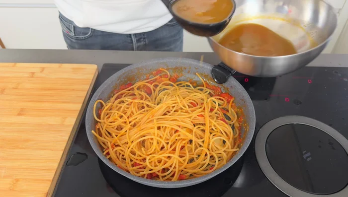 Add the partially cooked spaghetti to the pan with the shrimp broth and tomatoes. Stir and cook until the pasta is al dente, adding more broth if needed.