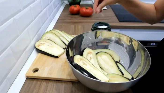 Place the eggplant slices in a container, sprinkle with salt, and stack them. Let them sit for at least an hour and a half, covered, to draw out bitterness.