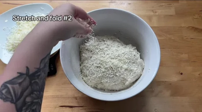 Perform the second set of stretch and folds, incorporating 50g of the grated cheese. Repeat the stretch and fold technique on all four sides. Set aside the remaining 30g of cheese.