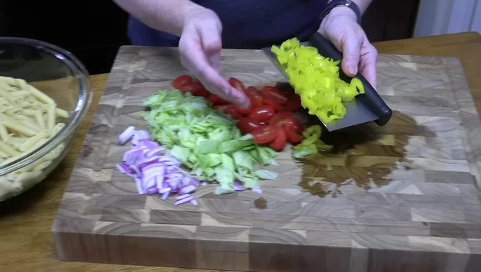 Combine cooked pasta, chopped vegetables, meats, and cheese in a large mixing bowl.