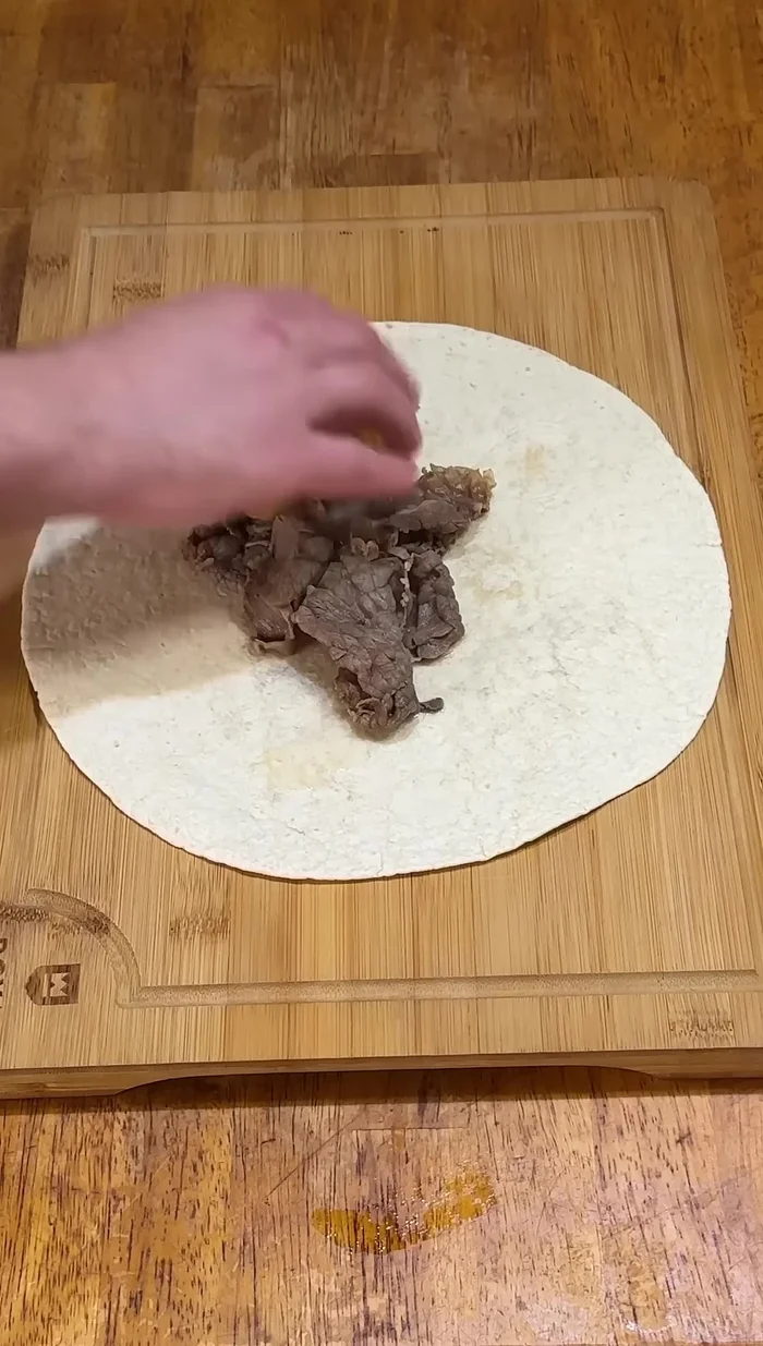 Add a generous amount of steaming hot Italian beef to the tortilla.