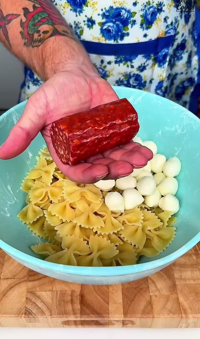 Add 8 oz of drained mozzarella pearls, 2 oz of chopped salami, 1/2 cup of chopped English cucumber, 1 cup of cherry or grape tomatoes, 1/2 of a diced red onion, and 1/2 jar of chopped roasted red peppers.