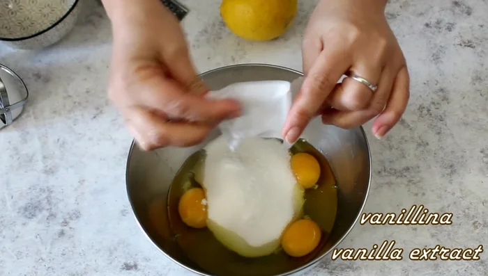 Add 170g sugar, a pinch of vanilla, and about half a lemon peel. Whisk until light and frothy.