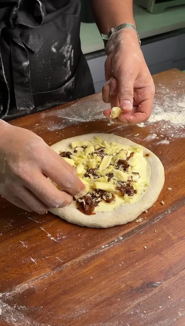 Assemble the pizza: Flatten the dough. Apply the cream sauce. Add paneer and caramelized onions. Top with mozzarella and cheddar cheese.