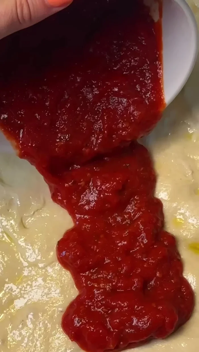 Spread a thick layer of cooled tomato sauce over the risen dough. Drizzle with olive oil, sprinkle with oregano and flaky sea salt.