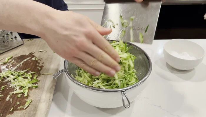 Place grated zucchini in a strainer over a bowl. Sprinkle with 1/4 teaspoon of salt and mix. Let sit for 10 minutes to draw out moisture.