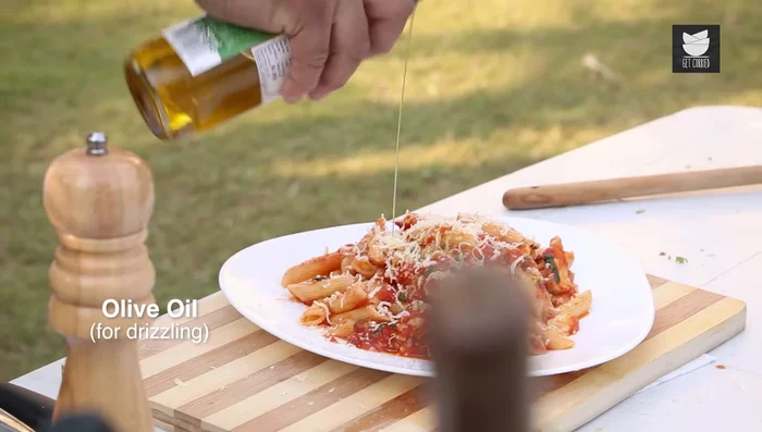 Serve the pasta, garnished with cheese, olive oil, basil, and olives.