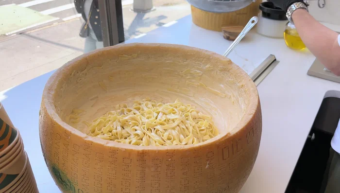 Add the pasta to a large Parmesan cheese wheel, mixing until the cheese melts and creates a creamy consistency.